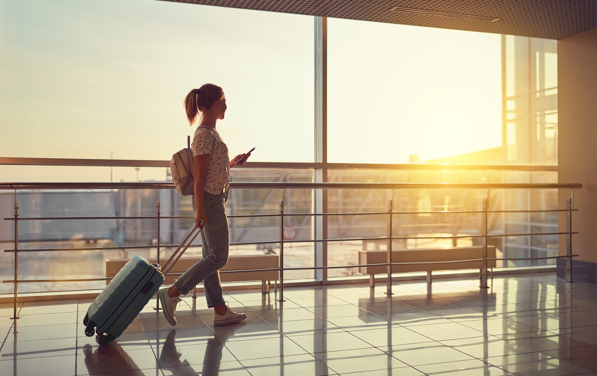 young woman goes  at airport at window with suitcase waiting for plane